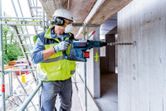 A person wearing safety equipment uses a cordless rotary hammer to drill into concrete.