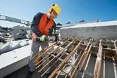 A person wearing safety equipment cuts rebar with a power tool at a construction site.