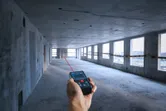 Person using a laser measure to determine distance in an unfinished concrete room.