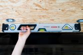 A person holds an optical level against a wooden ceiling for alignment.