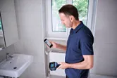 A person uses a thermo camera and a smartphone in a tiled bathroom.