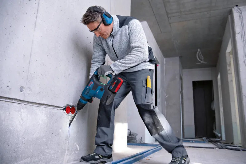 A person wearing safety equipment drills into a concrete wall in a construction area.