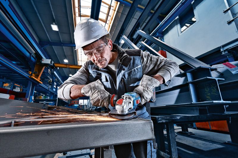 GWX 18V-15 SC A person wearing safety equipment grinds metal with a cordless angle grinder.
