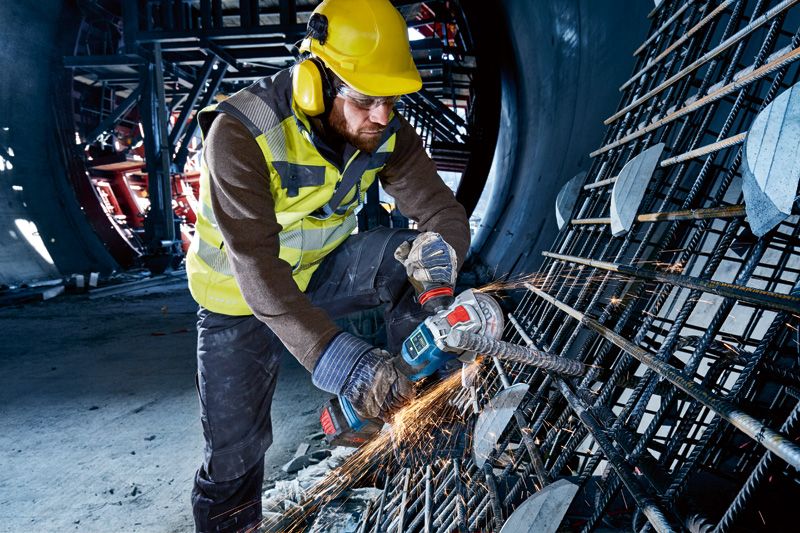 GWX 18V-15 SC A person wearing safety equipment uses a cordless angle grinder to cut rebar.