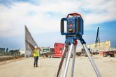 Laser leveling tool on tripod at a construction site, person wearing safety equipment in background.