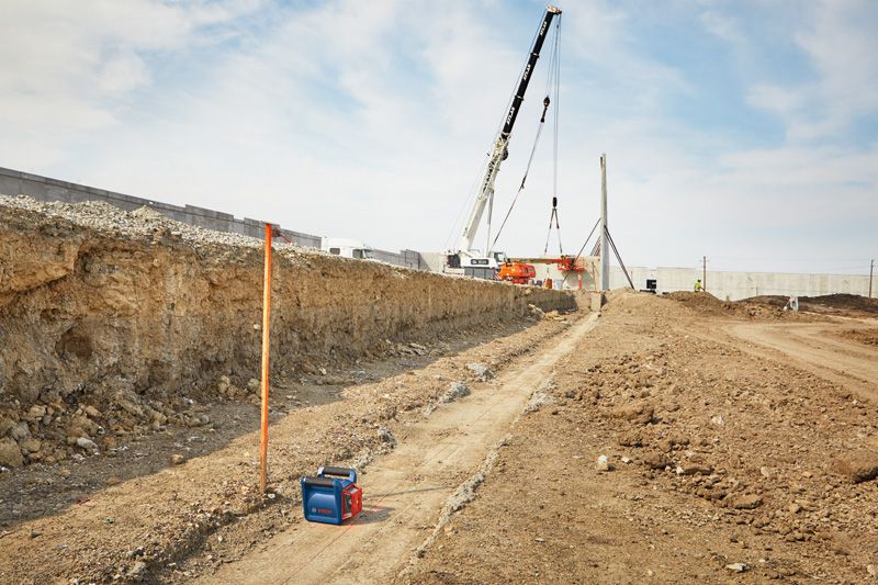 Laser leveling tool set up on a construction site with cranes and earthmoving in the background.
