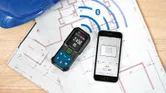 Laser measure and smartphone displaying measurements on construction blueprints.