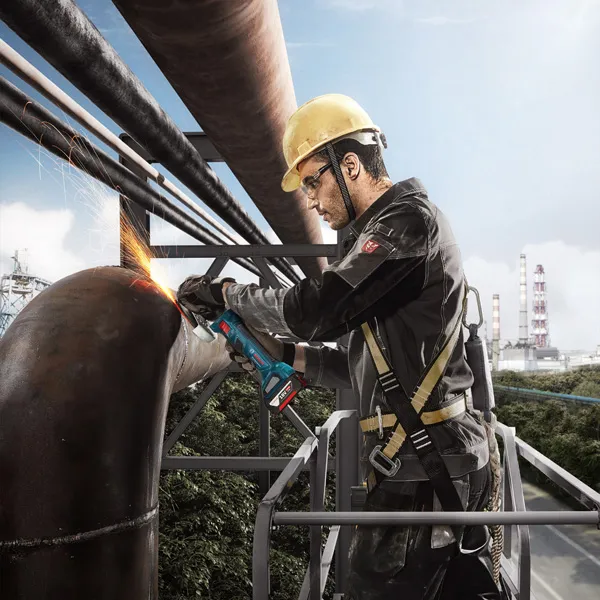 GWS 180-LI A person wearing safety equipment grinds a large metal pipe with an angle grinder.