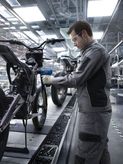 A person wearing safety equipment uses a power tool to assemble a motorcycle frame.