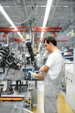 Person wearing safety equipment uses a power tool to assemble machinery on a factory line.