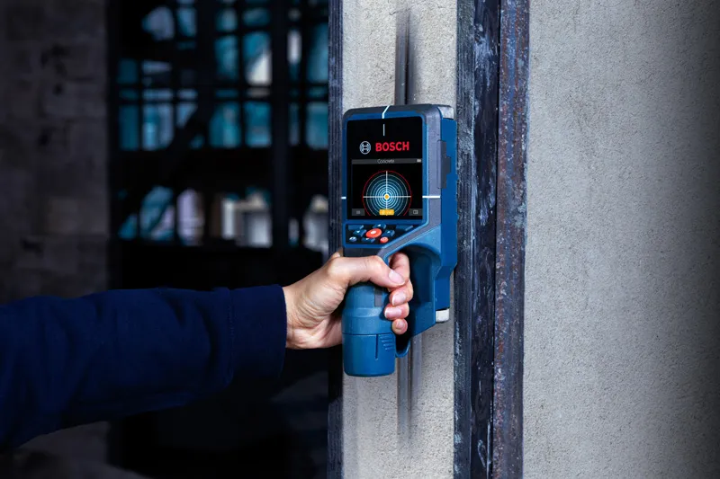 Person scanning a wall using a detector for hidden objects.