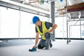 A person wearing safety equipment scans the floor of a construction site with a wall scanner.