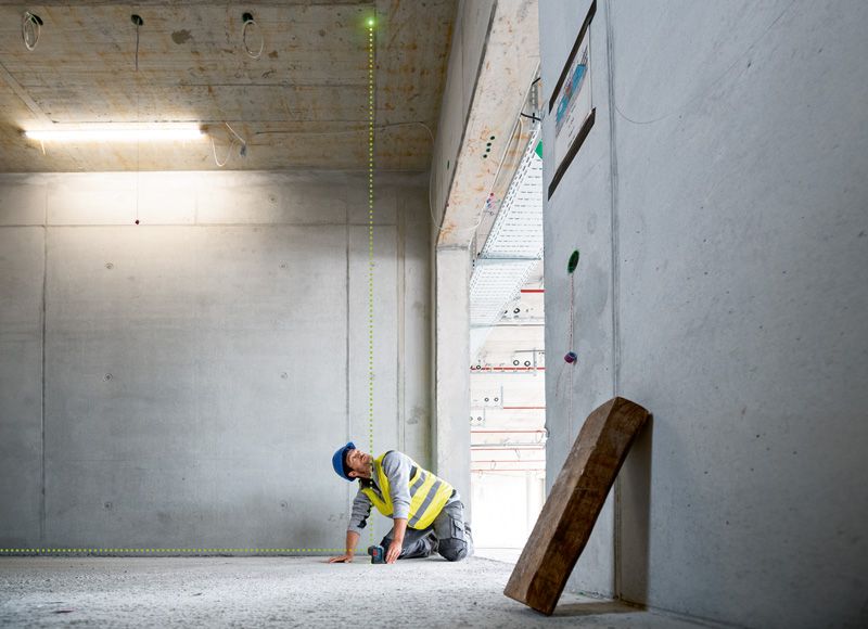 A person wearing safety equipment aligns a laser leveling tool on a concrete floor.