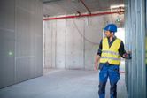 A person wearing safety equipment uses a laser leveling tool on a construction site.