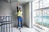 A person wearing safety equipment uses a point laser to mark the ceiling in a concrete room.