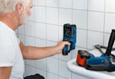 Person scans a tiled wall with an inspection tool in a workspace.