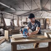 A person wearing safety equipment uses a router to shape wood in a workshop.
