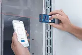 Person uses a laser measure and smartphone app to record measurements on a wall.