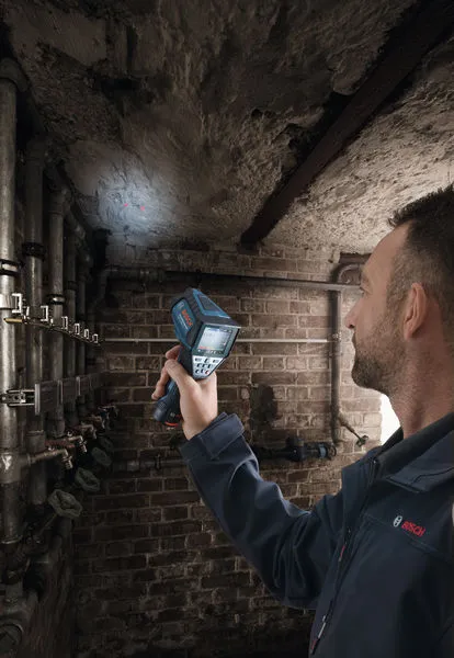 GIS 1000 C Person using a thermal camera to inspect pipes along a brick wall.