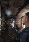 A person scans a brick wall with a thermo detector in a utility room.