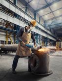 A person wearing safety equipment uses a power grinder to cut metal, creating sparks.