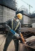A person wearing safety equipment grinds metal bars with an angle grinder at a construction site.