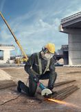 A person wearing safety equipment uses an angle grinder to cut metal rods at a construction site.
