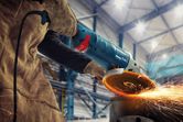 A person wearing safety equipment grinds metal, producing bright sparks in a workshop.