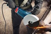 A person wearing safety equipment cuts metal rebar with an angle grinder, creating sparks.