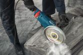 A person wearing safety equipment uses a power cutter to cut a concrete block.