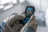 Person wearing safety equipment operates a laser measure with a digital display.