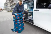 A person loads stacked toolboxes onto a dolly beside an open work van.