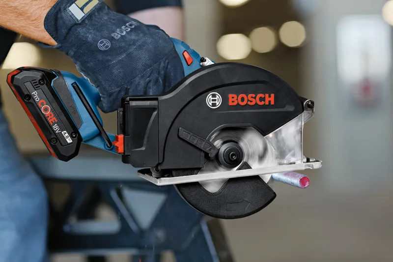 A person wearing safety equipment cuts a metal pipe with a cordless circular saw.