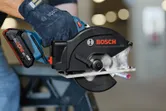 A person wearing safety equipment cuts a metal pipe with a cordless circular saw.