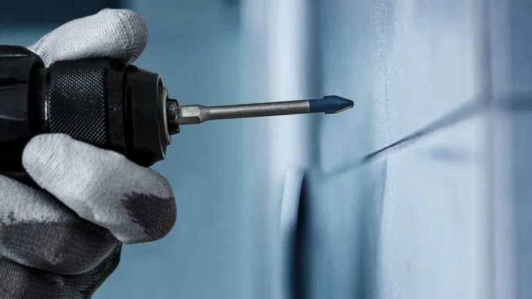 EXPERT Hard Ceramic HEX-9 Drill Bit Set, 5 x 90; 6 x 90; 8 x 90 mm, 3 pcs A person wearing safety equipment drills into a tiled wall.