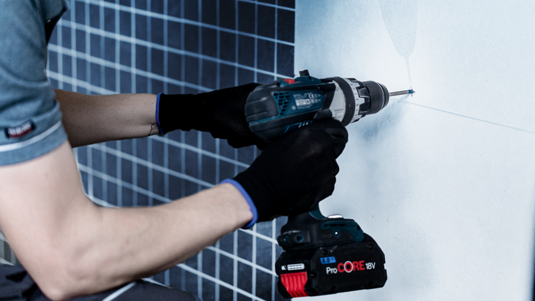 EXPERT Hard Ceramic HEX-9 Drill Bit Set, 5 x 90; 6 x 90; 8 x 90 mm, 3 pcs Person wearing safety equipment drills a screw into a tiled wall.