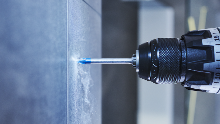 EXPERT Hard Ceramic HEX-9 Drill Bit Set, 5 x 90; 6 x 90; 8 x 90 mm, 3 pcs A power drill making a hole in a tiled wall.