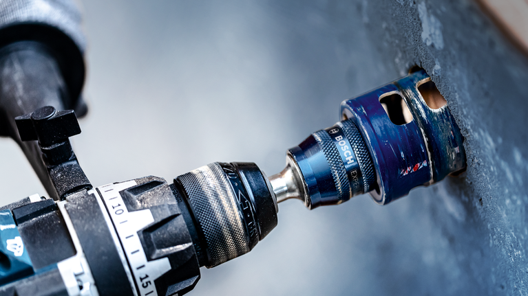 EXPERT Power Change Plus Hole Saw System Arbor 11 mm, TCT Drill 8.5 x 105 mm, 2-pc Drill with a hole saw attachment making a circular cut in a concrete wall.