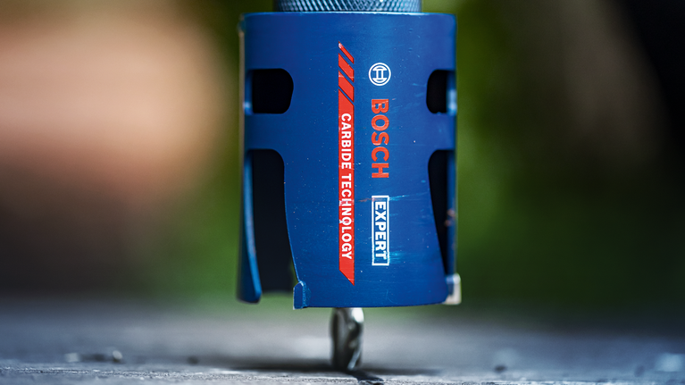 EXPERT Construction Material Hole Saw 68 x 60 mm Close-up of a blue carbide hole saw drilling into a flat surface.