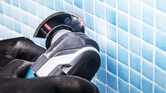 A person wearing safety equipment uses a rotary tool to cut blue wall tiles.