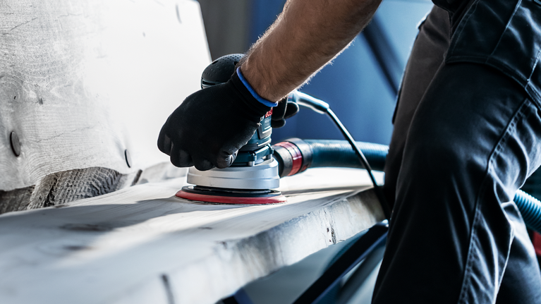 EXPERT M480 Starter Kit for Random Orbital Sanders 125 mm 7-pc Person wearing safety equipment sands a wooden plank with a power sander.