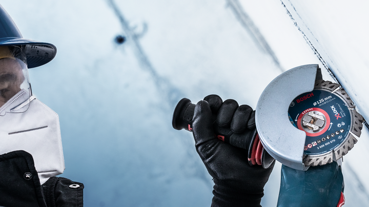 Object #200360655: 2793282_web_003 Person wearing safety equipment uses an angle grinder to cut a metal surface.