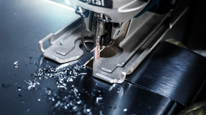 Jigsaw cutting a precise hole in a sheet of metal, surrounded by metal shavings.