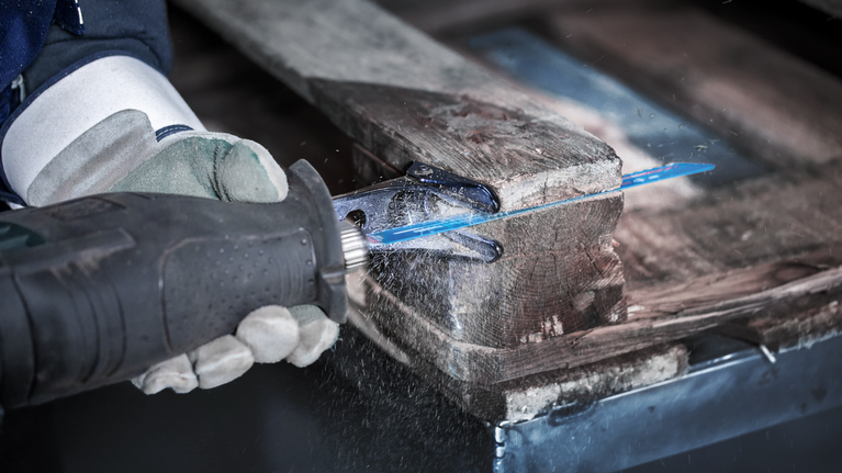 EXPERT Hard Nail Pallets S1122CHM Reciprocating Saw Blade 10-pc Person wearing safety equipment uses a reciprocating saw to cut through a wooden pallet.