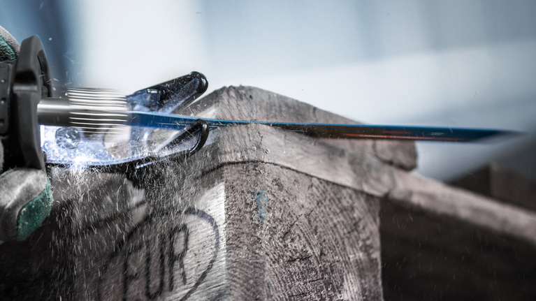 EXPERT Hard Nail Pallets S1122CHM Reciprocating Saw Blade 10-pc Person wearing safety equipment uses a reciprocating saw to cut through a wooden crate.