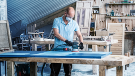 A person wearing safety equipment sands a blue door in a woodworking shop.
