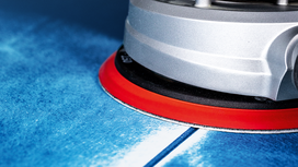 Orbital sander smoothing a blue surface.