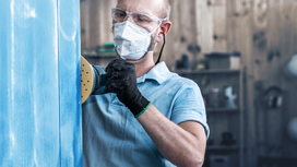 A person wearing safety equipment sands a blue surface with a power tool.