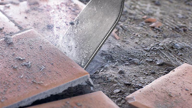 Tile chisel breaking ceramic tiles on a dusty floor.