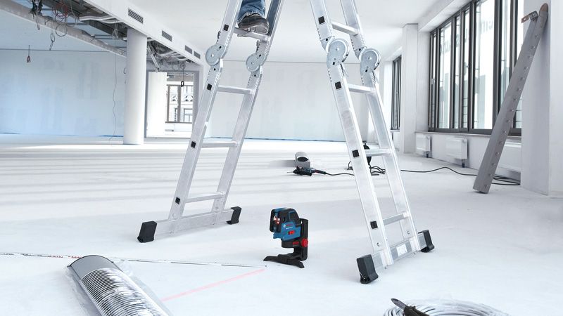 GCL 25 Laser leveling tool projecting lines on the floor beneath a person on a ladder.